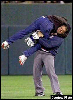 El árbitro Luis César Valdés aplica artes marciales para derribar a Diego Tintorero en el juego Cuba-Orioles, mayo de 1999.